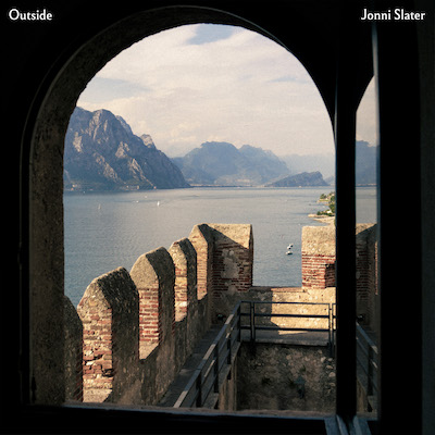 Cover image for Outside single, an open window in a dark room looking out onto castle walls, a lake and mountains in the distance.