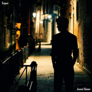 Cover image of the single Super. A silhouetted figure of Jonni Slater standing in a darkened street in Venice, with streetlights creating pools of light along the cobbled walkway that recedes into the distance.